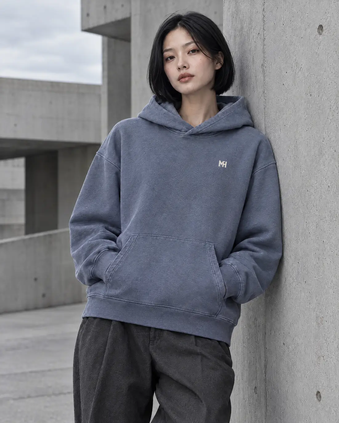 Streetwear movement campaign: a woman with a black bob in a slate-blue washed hoodie with a small embroidered MH monogram