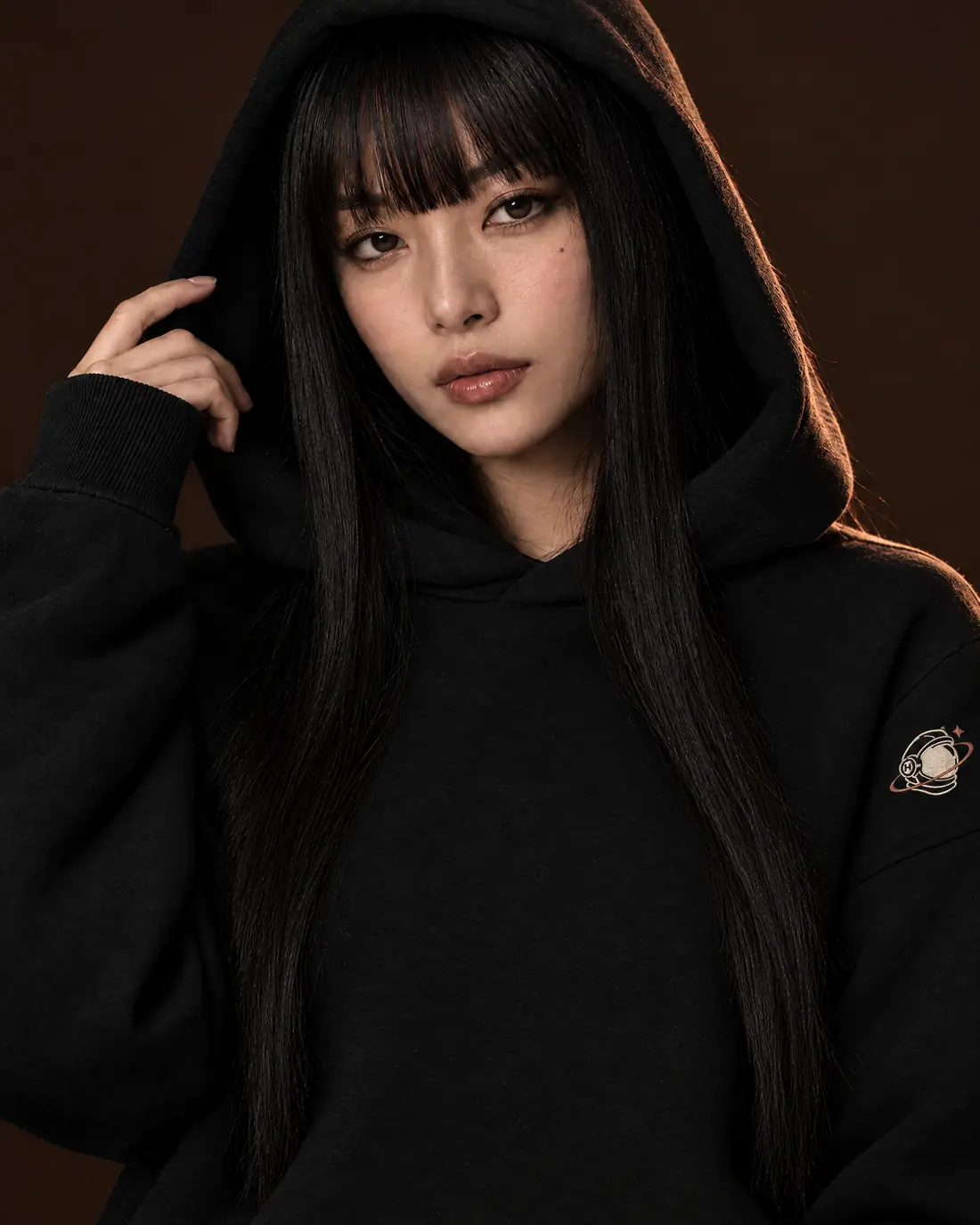 Streetwear movement: a woman with long black hair, hood up, in a black hoodie with the MH astronaut embroidered on the upper sleeve