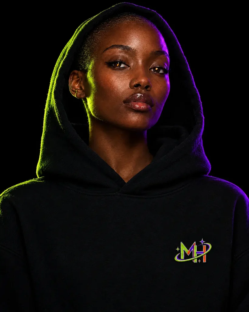 Woman with a shaved head, hood up, lit by purple and lime neon, with the neon MH monogram on the left chest
