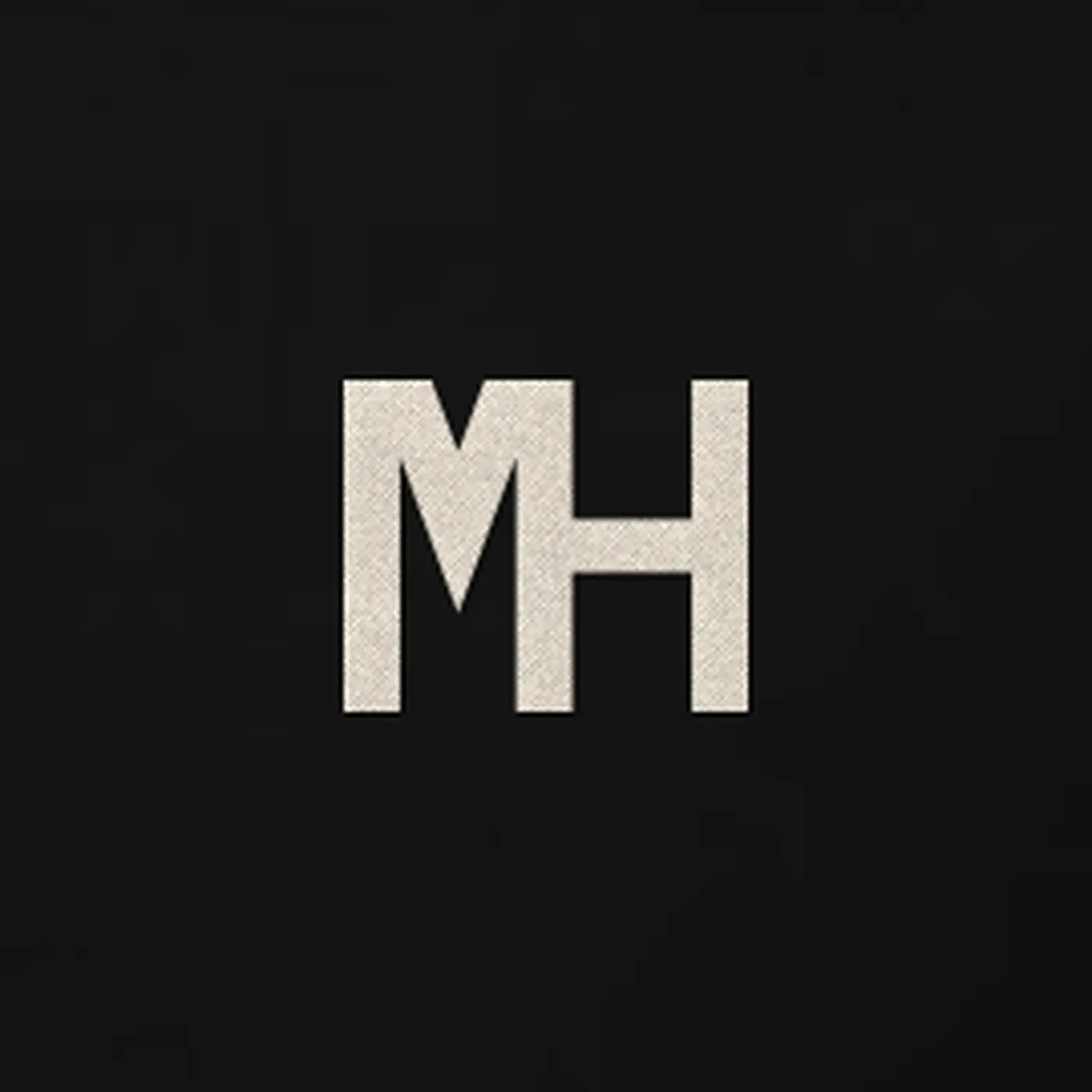 Close-up of a small cream MH monogram embroidered on the MH Relaxed Hoodie